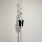Extra-long natural cotton macramé plant hanger holding a black nursery pot against a white wall, total length 1.43 metres.