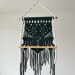 Green macramé wall hanging with wooden shelf and fringe detailing, suitable for 9–12cm indoor plant pots, displayed against a white wall.