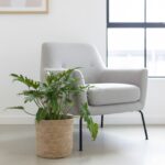 Extra large natural seagrass woven plant basket with green plant standing on white floor next to chair