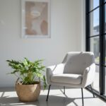 Extra-large round natural seagrass woven basket with upright handles with a green plant in it on a light grey floor next to a light grey one seater modern chair