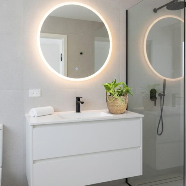 Small round natural seagrass woven basket with upright woven handles and plant in on white counter in modern bathroom