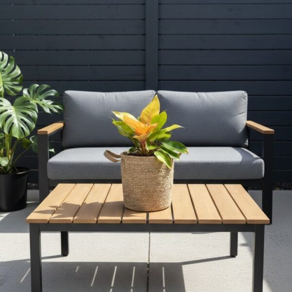 Large natural seagrass woven basket with brown handles and plant with orange leaves on a coffee table in an outdoor seating area